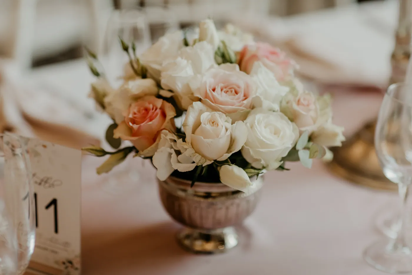 A blush and white rose bouquet beside a table number card.