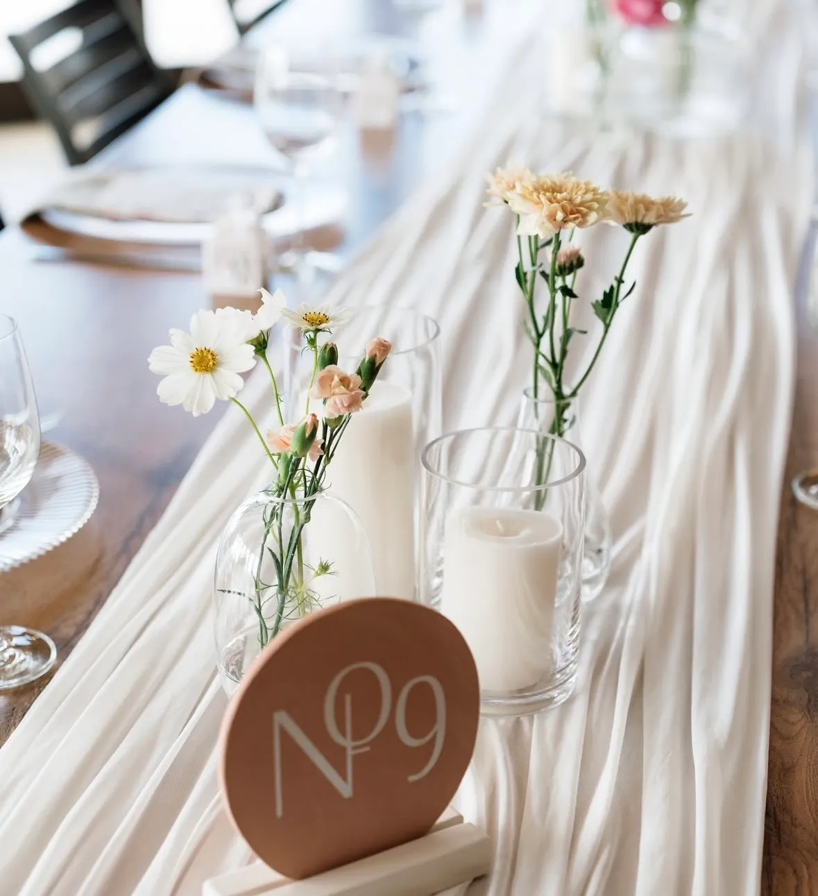 A linen table runner with candles and a wooden table number.