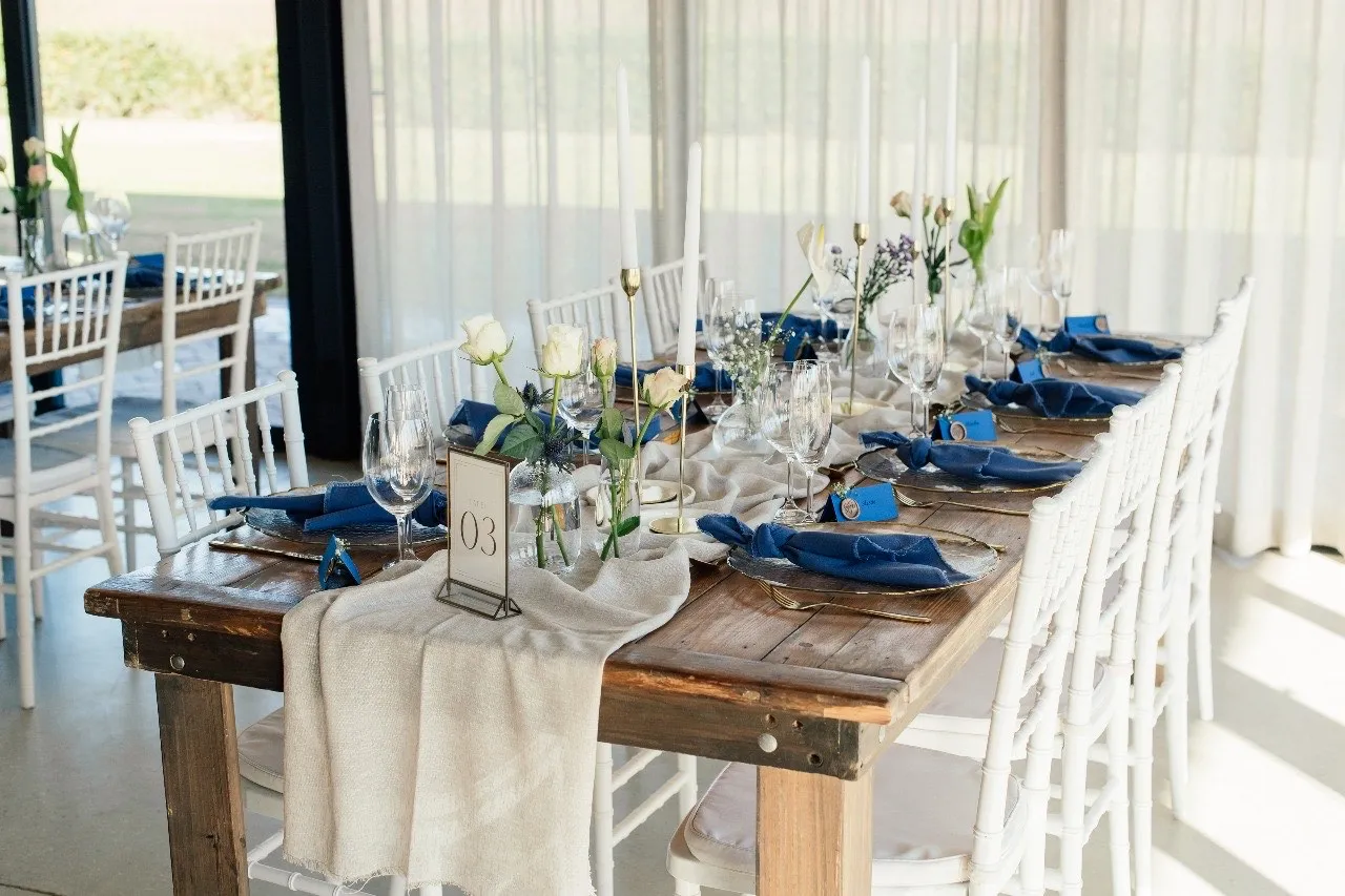 A navy linen table setting with white roses and gold candlesticks.