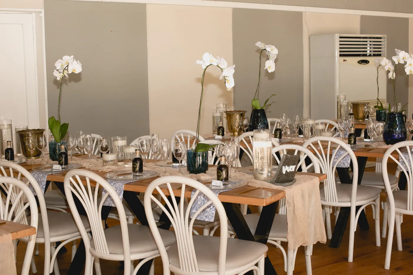 A wide view of a reception hall with orchid centerpieces along long tables.