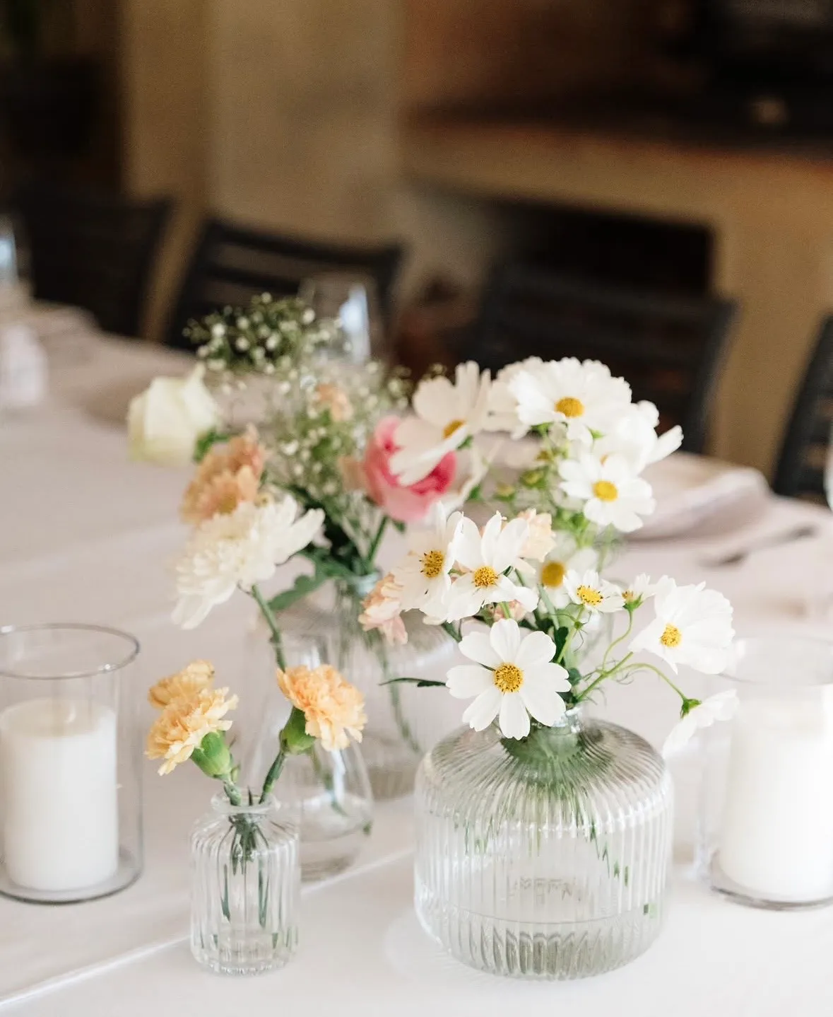 A close-up of mixed bud vase florals on a white table setting.